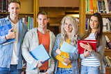 Students with folders standing against bookshelf in library