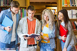 Students reading book against bookshelf in library