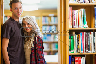 Smiling young couple by bookshelf in library