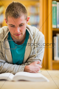 Male student reading book on the college library floor