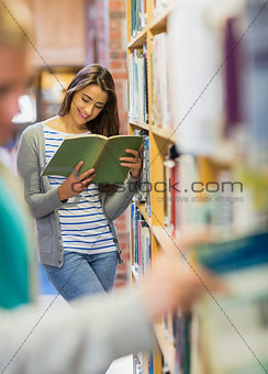 Student reading a book by bookshelf in the library