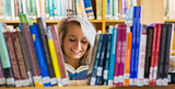 Smiling female student reading book in the library