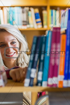 Smiling female student selecting book in the library