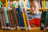 Student reading a book amid bookshelves in the library