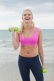 Cheerful sporty woman with dumbbells on beach