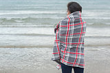 Rear view of woman covered with blanket looking at sea on beach