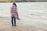 Rear view of woman covered with blanket looking at sea on beach