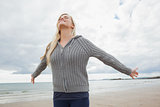 Woman in gray knitted jacket stretching arms on beach