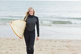 Smiling woman in wet suit holding surfboard at beach