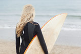 Rear view of woman in wet suit holding surfboard at beach