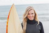 Smiling woman in wet suit holding surfboard at beach