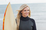 Smiling woman in wet suit with surfboard at beach