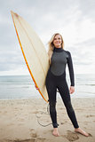 Smiling young woman in wet suit holding surfboard at beach