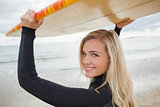 Smiling woman in wet suit holding surfboard over head at beach