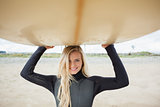 Smiling woman in wet suit holding surfboard over head