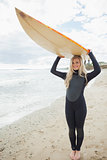 Woman in wet suit holding surfboard over head at beach