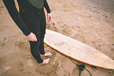 Low section of woman in wet suit with surfboard at beach