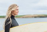 Side view of woman in wet suit holding surfboard at beach