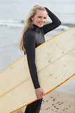 Beautiful young woman in wet suit holding surfboard at beach