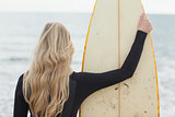 Rear view of a blond in wet suit with surfboard at beach