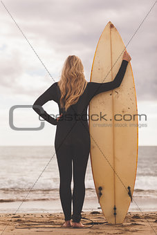 Rear view of a blond in wet suit with surfboard at beach