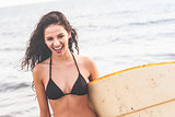 Cheerful bikini woman holding surfboard at beach