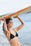 Bikini woman holding surfboard over head at beach