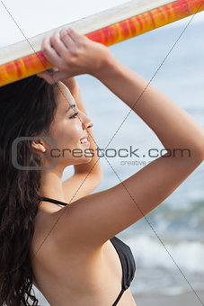 Bikini woman holding surfboard over head at beach