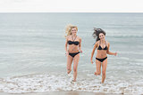 Smiling bikini women running in water at beach
