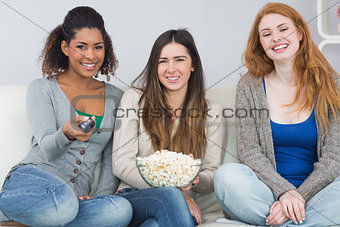 Female friends with remote control and popcorn bowl on sofa