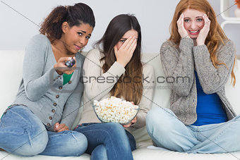 Scared friends with remote control and popcorn bowl on sofa