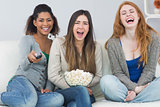 Cheerful friends with remote control and popcorn bowl on sofa