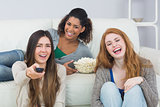 Cheerful friends with remote control and popcorn bowl at home