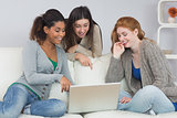 Cheerful female friends using laptop together at home