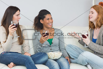 Cheerful friends with wine glasses and popcorn enjoying a conversation at home