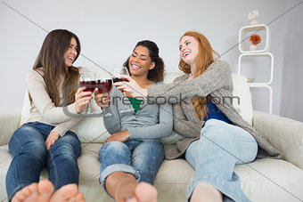 Cheerful female friends toasting wine glasses at home