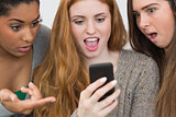 Shocked female friends looking at mobile phone together