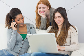 Happy young female friends using laptop and cellphone