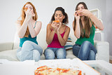 Happy young female friends eating pizza at home