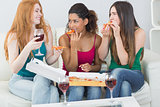 Happy female friends eating pizza with wine at home