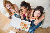 Happy young female friends with pizza and wine on sofa