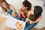 Overhead view of happy friends eating pizza with wine on sofa
