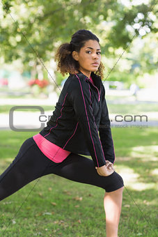 Serious healthy woman doing stretching exercise in park