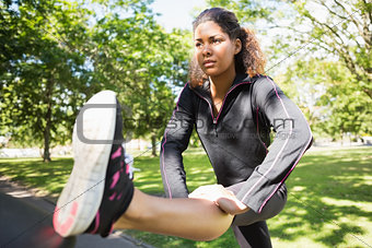 Sporty woman stretching her leg while standing in park
