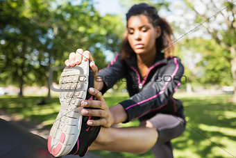 Pretty sporty woman stretching her leg in park