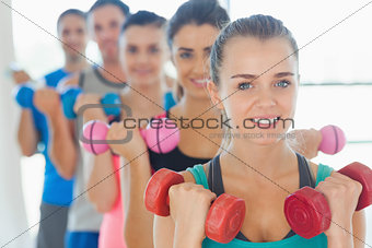 People lifting dumbbell weights with trainer in gym
