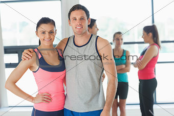Fit couple with friends standing in background in exercise room