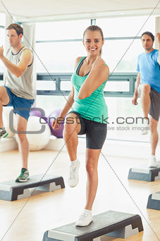 Instructor with fitness class performing step aerobics exercise