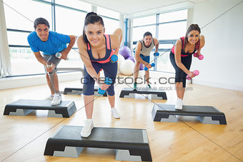 Instructor with fitness class performing step aerobics exercise with dumbbells
