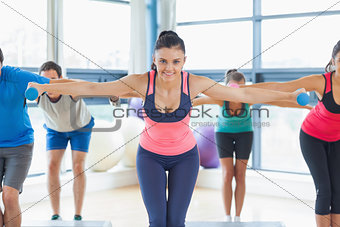 Instructor with fitness class performing step aerobics exercise with dumbbells
